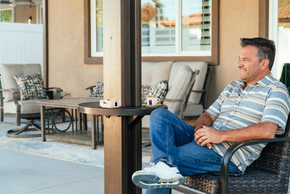 smiling man sitting next to his Alumatable patio post table with a drink